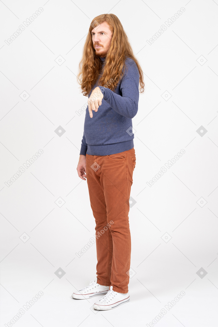 Vista lateral de um jovem em roupas casuais, apontando para baixo com um dedo