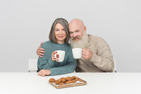 Envelhecido casal sentado à mesa e segurando copos de café