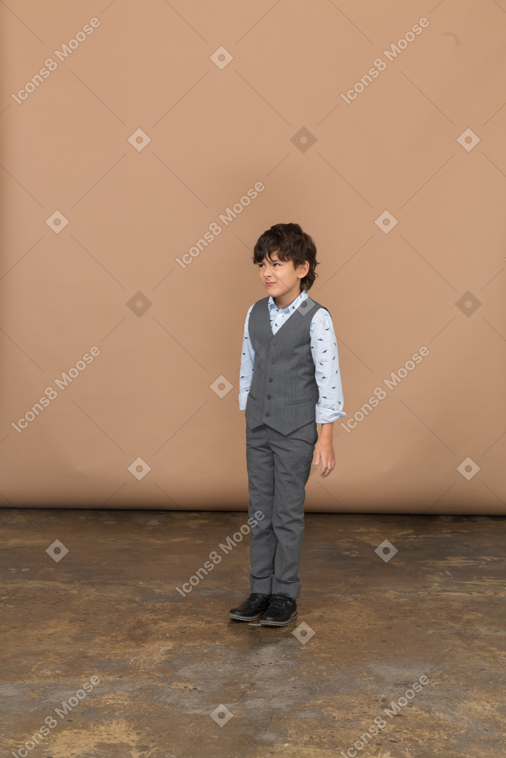 Vista frontal de un chico lindo en traje de pie con los puños cerrados y mirando a la cámara