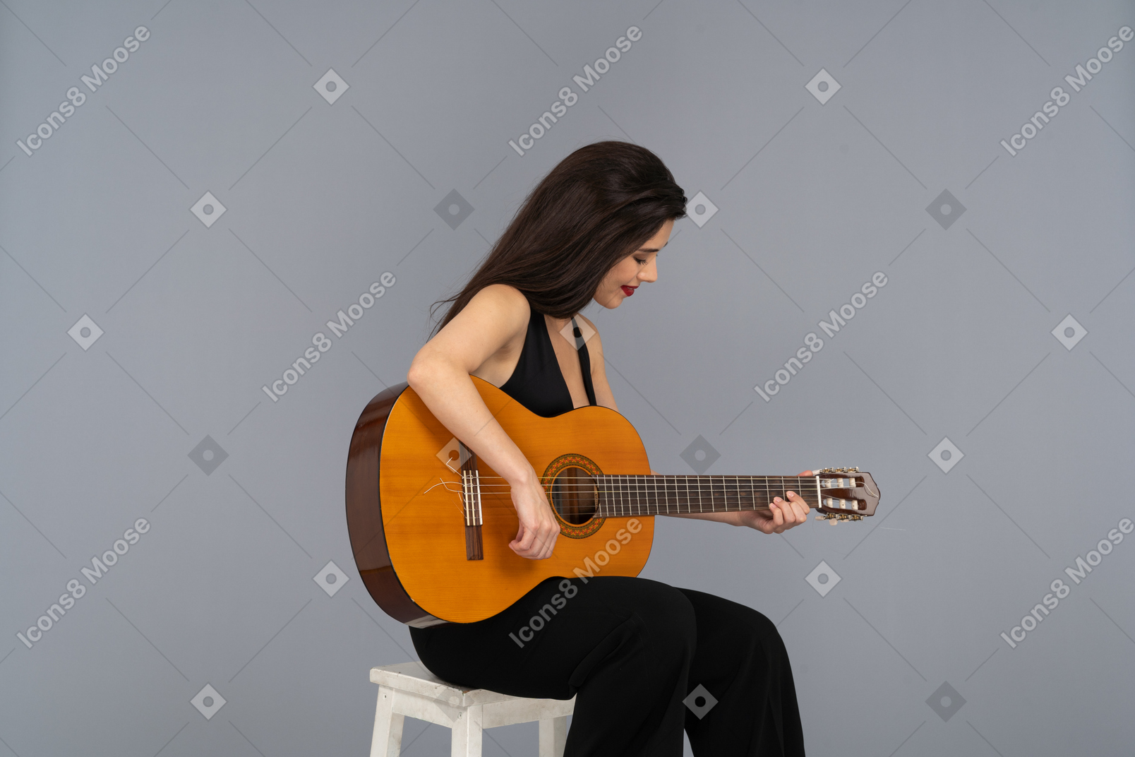 Three-quarter view of a sitting young lady in black suit playing guitar and looking down