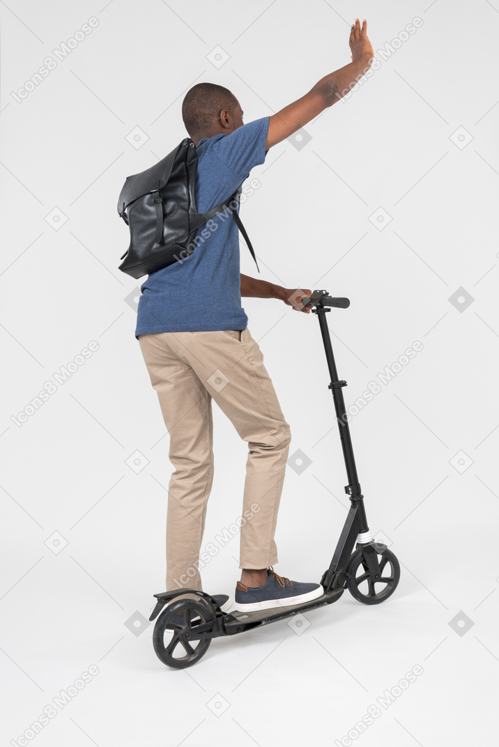 Black male city tourist standing back to camera on scooter and waving
