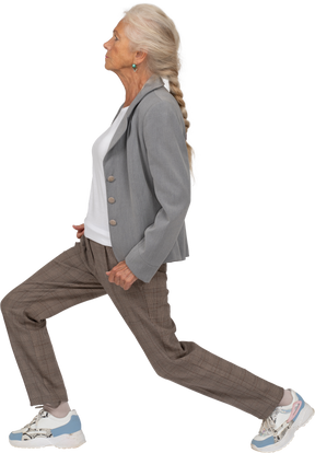 Side view of an old lady in suit doing forward lunges