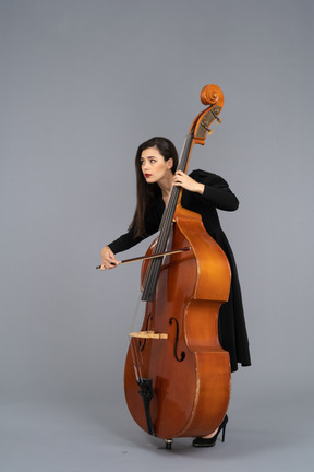 Three-quarter view of a young woman in black dress playing the double-bass with a bow