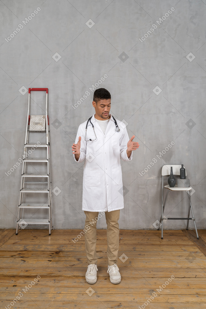 뭔가의 크기를 보여주는 사다리와 의자 방에 서있는 젊은 의사의 전면보기