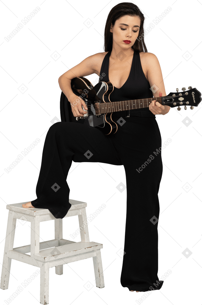 一位年轻的女士，穿着黑色西装，拿着吉他，把腿放在凳子上的前视图