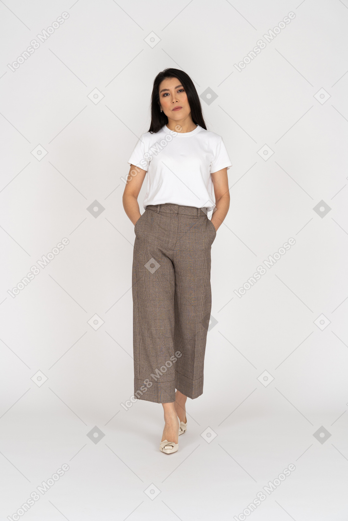 Front view of a walking bored young lady in breeches and t-shirt putting hands in pockets