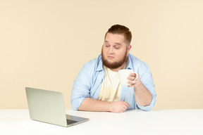 Interesado en algo joven con sobrepeso sentado frente a la computadora portátil y tomar el té