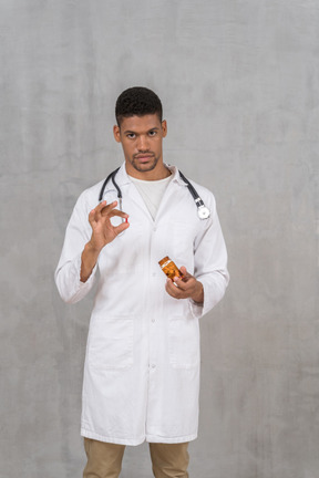 Young male doctor with stethoscope holding a pill