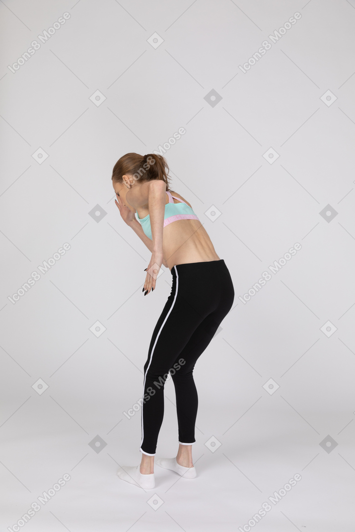 Three-quarter back view of a teen girl in sportswear leaning forward while standing like a robot