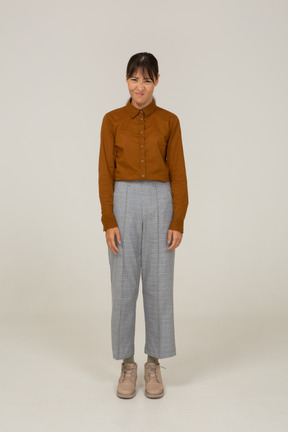 Front view of a grimacing young asian female in breeches and blouse standing still