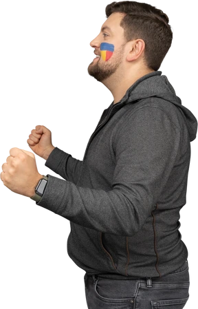 Side view of a satisfied male football fan with colorful face art clenching fists