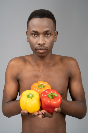 A shirtless young man holding bell peppers