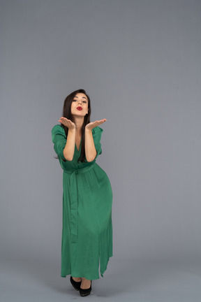 Vista frontal de una joven en vestido verde enviando un beso al aire