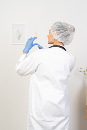 Back view of a young female doctor holding a syringe