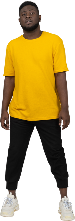Vista frontale di un giovane uomo dalla pelle scura in maglietta gialla che sta fermo
