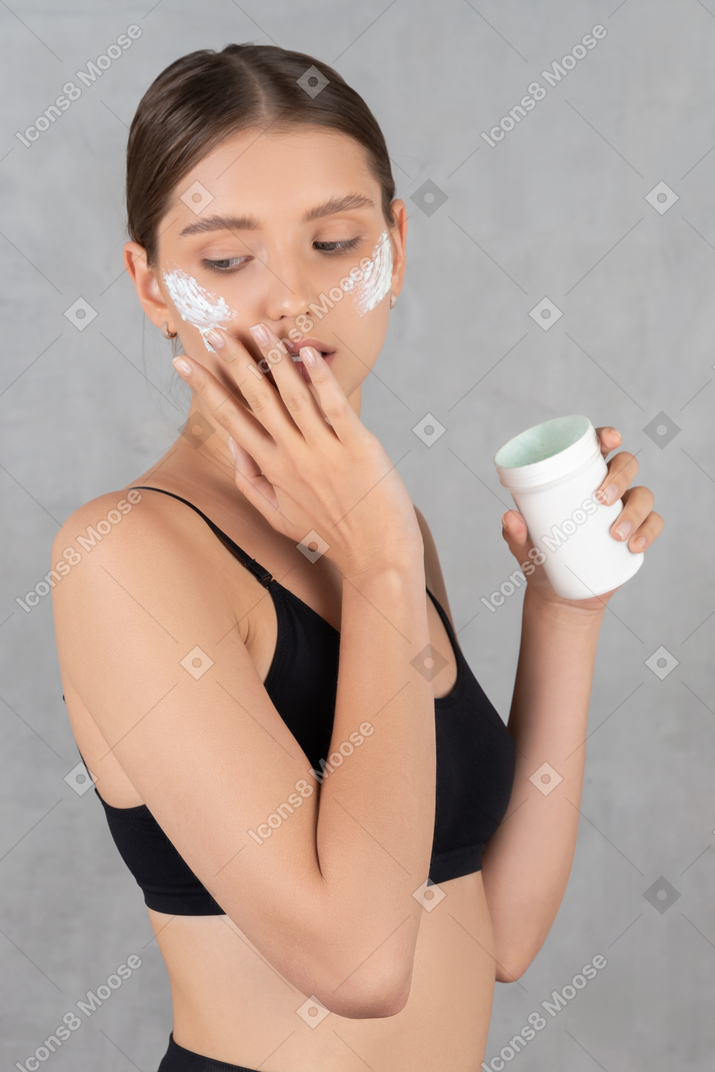 Woman looking down while applying face cream on her skin
