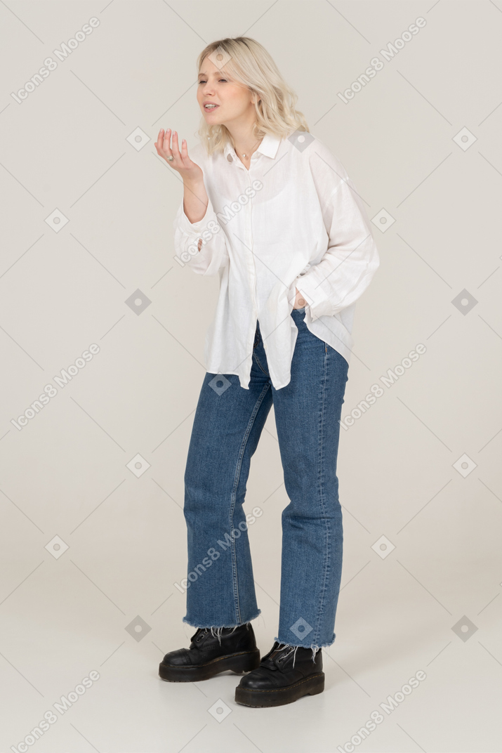 Three-quarter view of a young female in casual clothes putting hands in pocket while talking and gesticulating