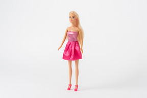 A front shot of a barbie doll in a shiny pink dress and pink high heels, standing isolated against a plain white background