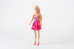 Eine vorderansicht einer barbie-puppe in einem glänzenden rosa kleid und rosa high heels, stehend vor einem einfachen weißen hintergrund isoliert