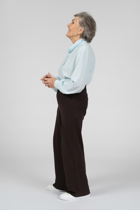 Vista laterale di una donna anziana sorridente con le mani giunte