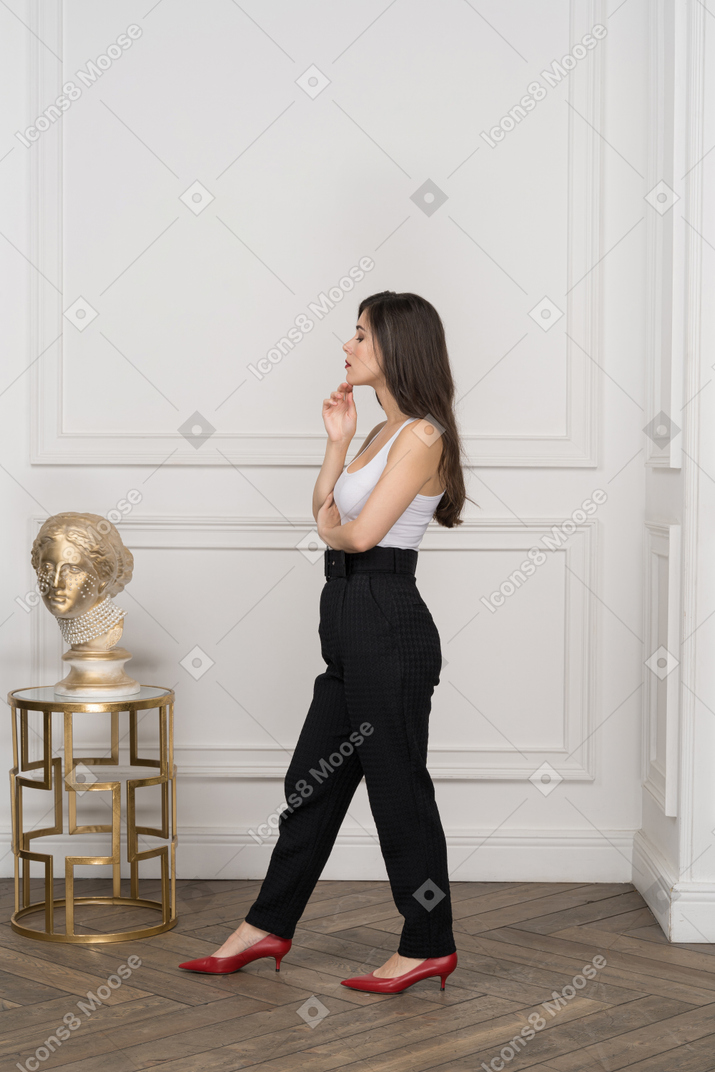 Вид сбоку молодой женщины, задумчиво смотрящей на золотую греческую скульптуру