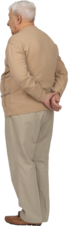 後ろ手で立っているカジュアルな服装の老人の背面図