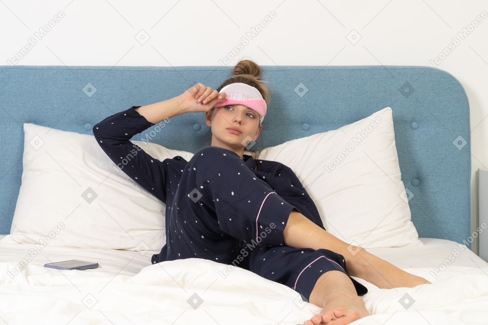 Front view of a laying young lady in pajamas putting on sleeping mask