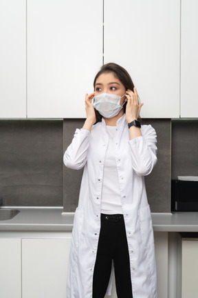 Vista frontale di una dottoressa che regola la sua maschera protettiva e che osserva da parte