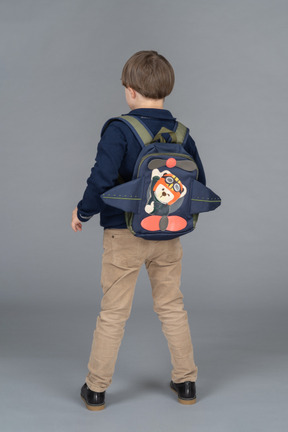 Little boy with a backpack standing with his back to camera