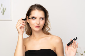 Front view of a smiling young woman wearing black top applying mascara