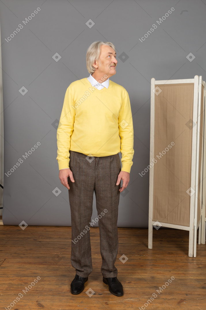 Front view of an old man in a yellow pullover turning his head while looking up