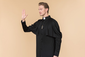 Catholic priest standing half sideways with his hand up