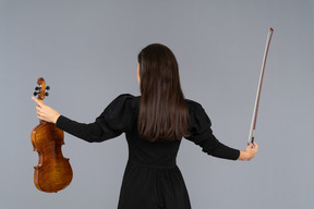 Vista de trás de uma violinista em vestido preto estendendo as mãos