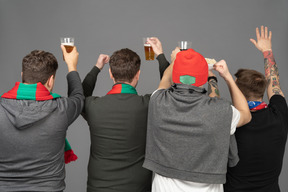 Vista posterior de cuatro fanáticos del fútbol masculino celebrando la victoria y sosteniendo cerveza