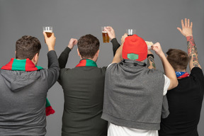 Back view of four male football fans celebrating the victory & holding beer