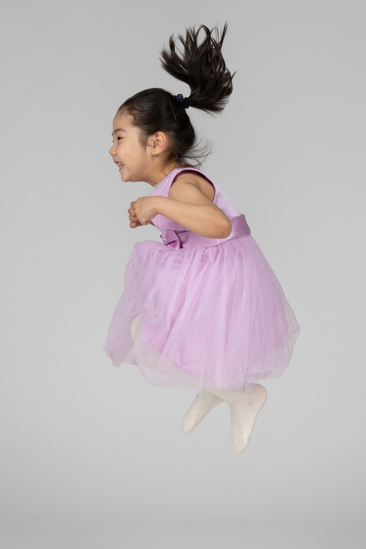 Girl in a pink dress jumping with her legs folded