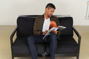 Lindo jovem sentado em um sofá segurando uma revista