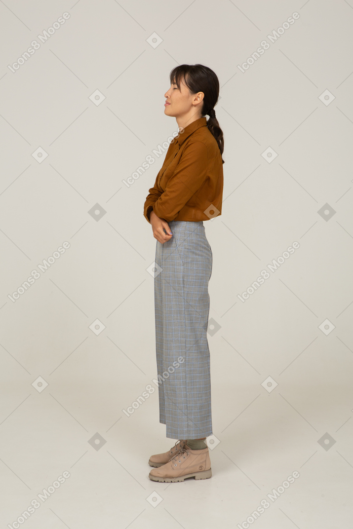 Side view of a tired young asian female in breeches and blouse crossing arms