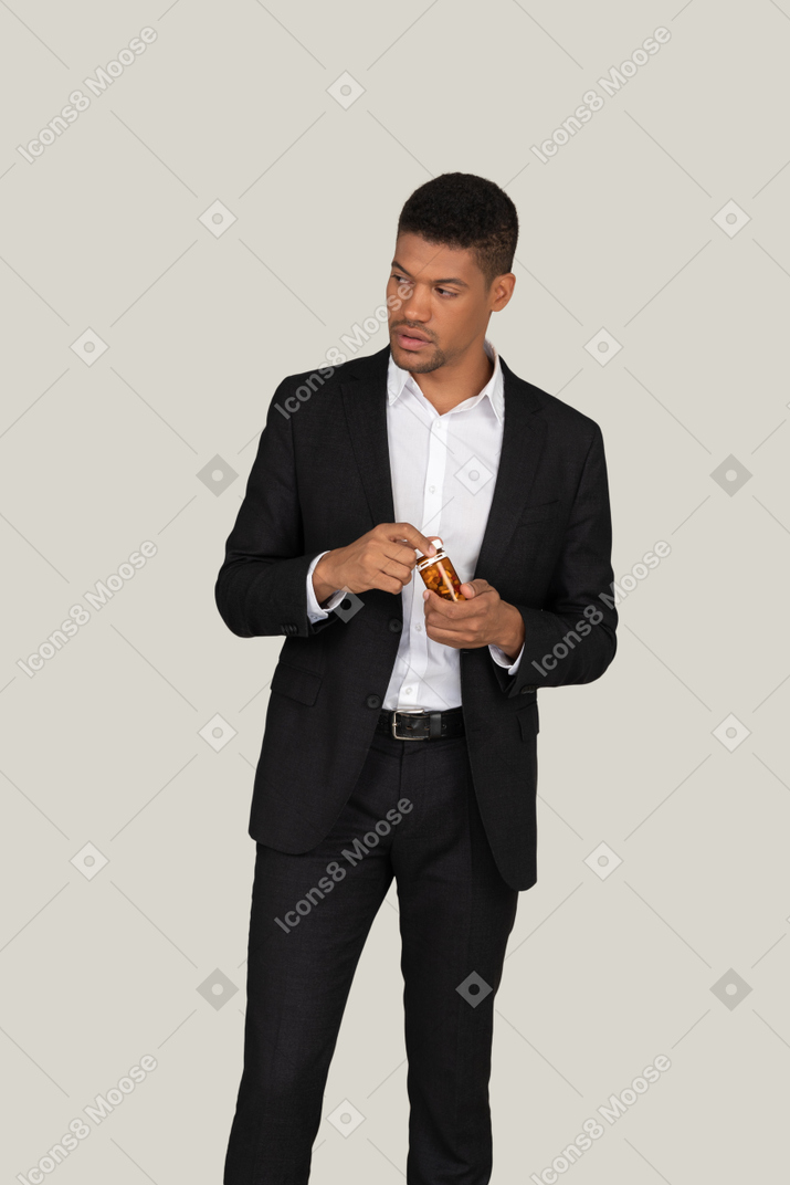 Pensive young man in black suit holding bottle of pills