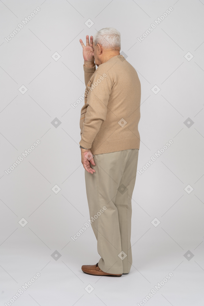 一位穿着休闲服的老人透过手指看的侧视图
