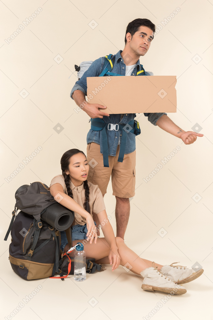 Young interracial couple of hitchhikers figuring out something