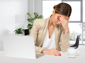 A woman sitting at a desk and holding her head