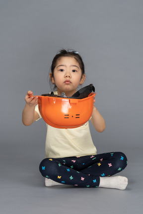 Vista frontal de uma menina segurando um capacete laranja