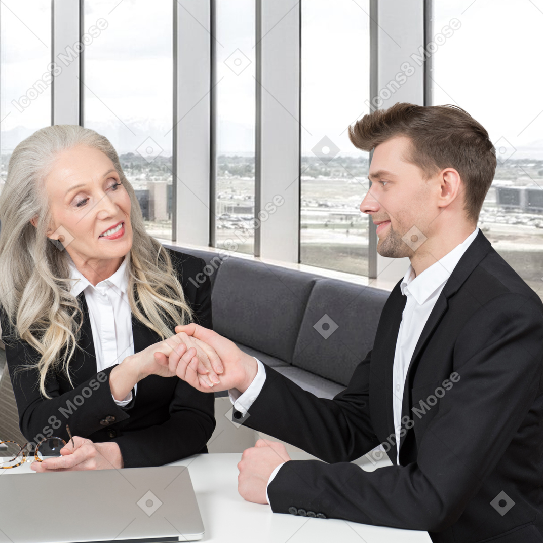 A businessman and a businesswoman shaking hands at a table