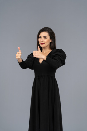 Dreiviertelansicht einer lächelnden jungen dame in einem schwarzen kleid, das daumen hoch zeigt
