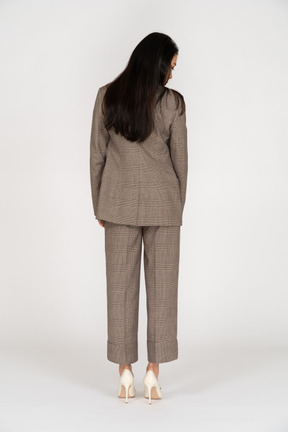 Back view of a young lady in brown business suit turning head