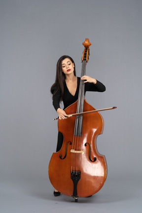 Front view of a young woman in black dress playing the double-bass with a bow