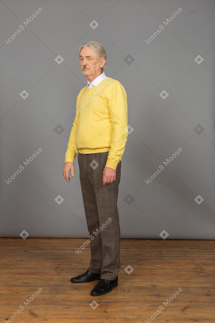 Трехчетвертный вид любопытного старика в желтом пуловере, поворачивающего голову и подмигивающего