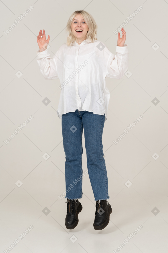 Front view of a surprised young female in casual clothes jumping and raising hands