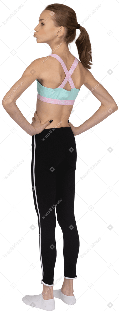 Vista posteriore di tre quarti di una ragazza adolescente in abbigliamento sportivo che soffia sulle guance e mette le mani sui fianchi